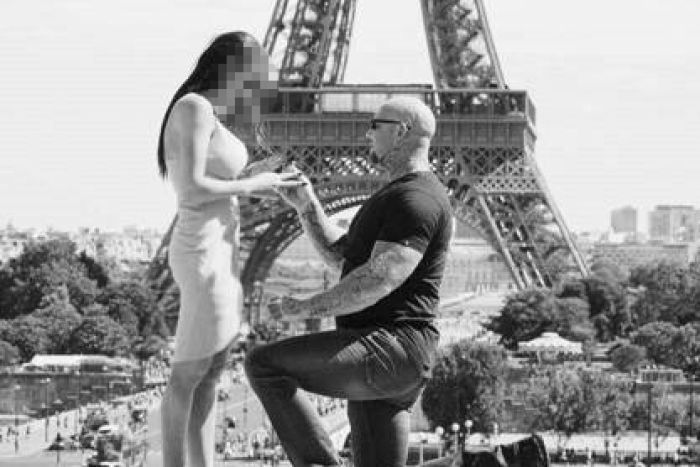 Leigh Slater kneels in front of a woman, appearing to propose. The Eiffel Tower is in the background.